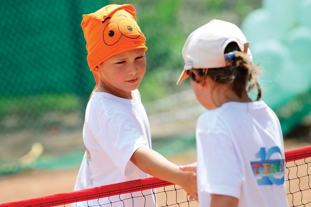 Doi copii își dau mâna la fileu după un meci Tenis10
